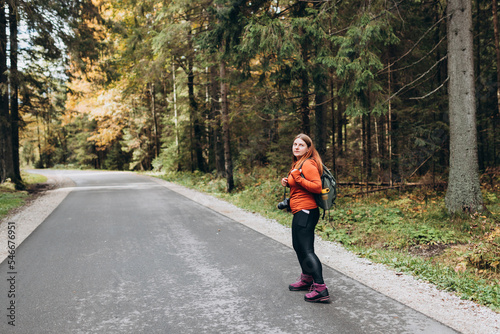 Solo tourist Woman hiking on footpath in autumn forest. Full body photo. Happy redhead person in active trekking clothes walking on nature backgraund. Travel and active lifestyle concept.