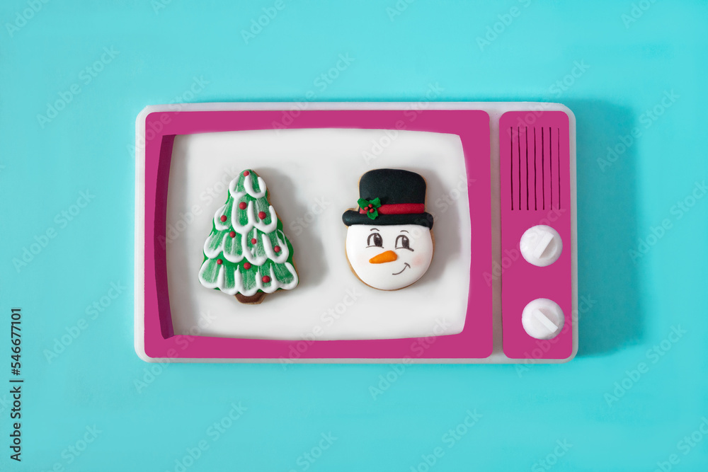 A Christmas tree and a snowman on the white screen of a retro tv with magenta frame against blue background. Surreal concept for romantic Christmas movies on television in winter time. A Christmas tree and a snowman on the white screen of a retro tv with magenta frame against blue background. Surreal concept for romantic Christmas movies on television in winter time.