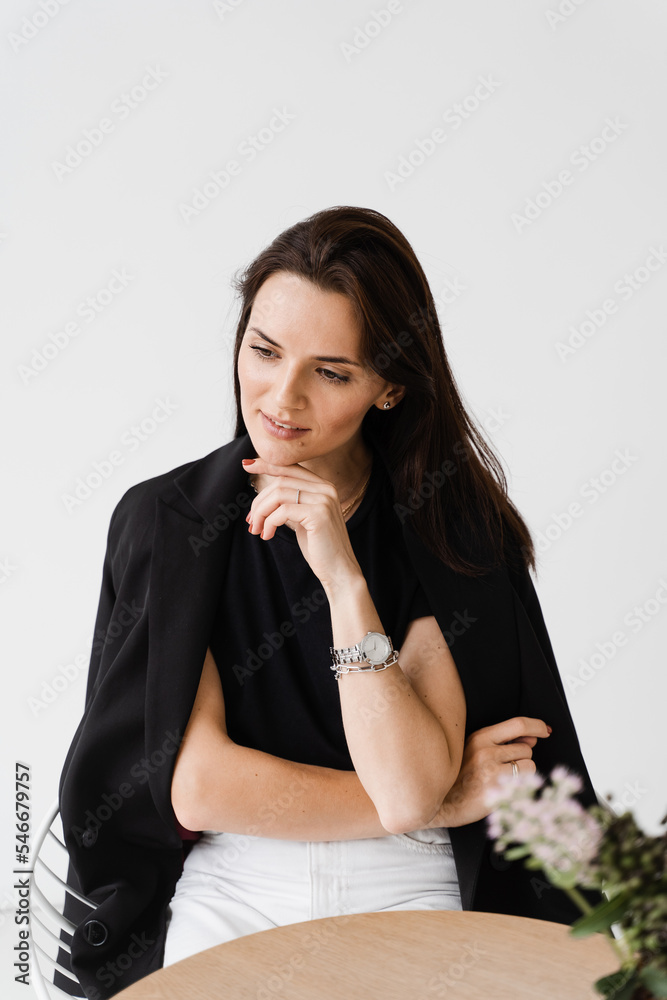 Portrait of attractive young woman on white background. Dreamy cheerful girl dressed in business style is sitting at table in white cafe. Portrait of attractive young woman on white background. Dreamy cheerful girl dressed in business style is sitting at table in white cafe.