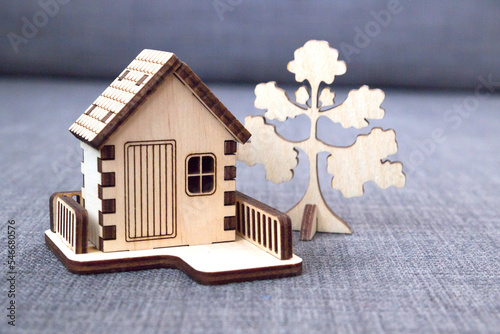 Wooden decorative toy house with a fence and a tree standing on a gray background.