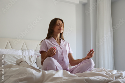 Young woman meditating in her bed in the morning. Yogini practicing meditation in the comfort of her bedroom. Background, copy space.