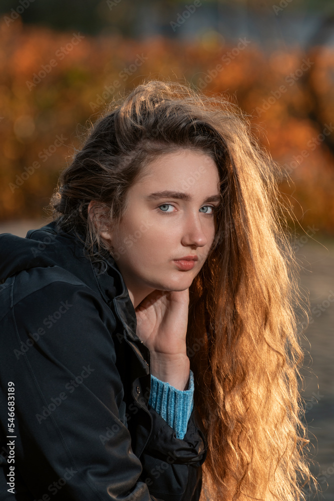 Young woman with long chestnut thick curly hair looks into the camera. Girl with auburn wavy hair. Young woman with long chestnut thick curly hair looks into the camera. Girl with auburn wavy hair.