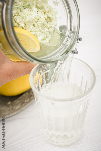 A stream of lemonade from a bottle of liqueur from elderberry flowers pouring into a faceted glass. Medicine with elderberry flowers. A cool refreshing summer drink photo