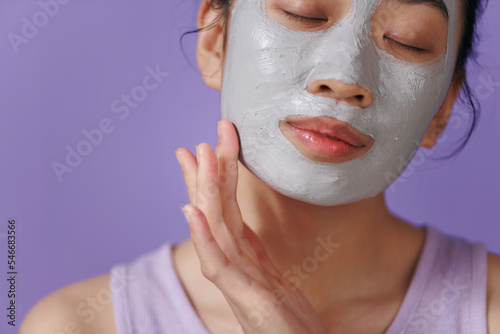 Young woman applying facial gray mud clay mask to her face