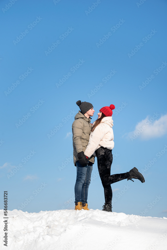 Happy young couple is walking on winter day. Couple in love against blue sky on snowy hill
