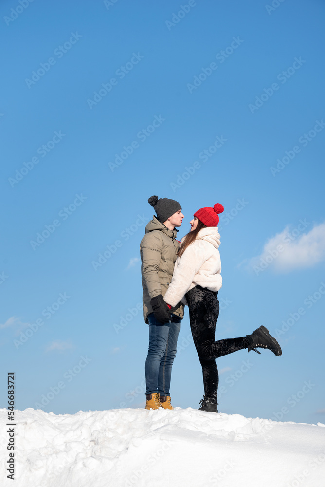 Happy young couple is walking on winter day. Couple in love against blue sky on snowy hill Happy young couple is walking on winter day. Couple in love against blue sky on snowy hill