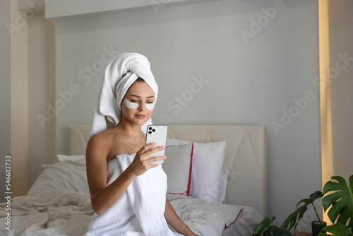 Young woman wearing a towel after showering recording a video review of the under eye patch for dark circles treatment for her beauty blog. Close up, copy space, background.