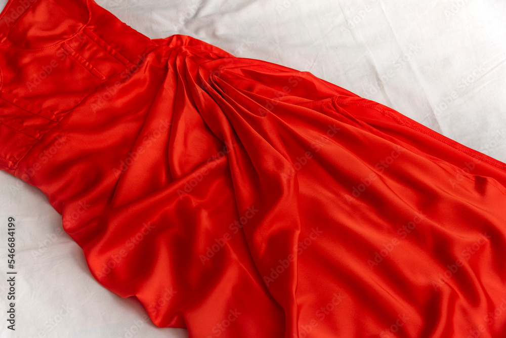 Details of satin red elegant dress. Women's dress made of silk on white background. Evening outfit. Wave texture