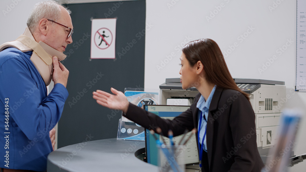 Obraz premium Asian receptionist helping patient with cervical neck foam at reception counter in health center. Facility worker giving support to old man with medical collar after injury, healthcace nisurance.