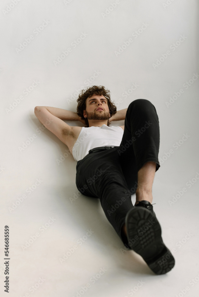 A guy with messy hair lays thoughtfully in on the floor