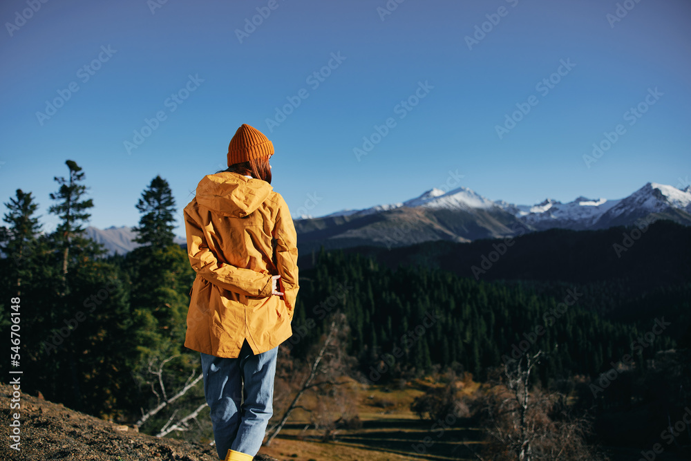 Woman full-length hiker standing frozen on the mountain looking at nature happiness with a view of the mountains in a yellow raincoat travel and hiking in the mountains at sunset freedom Woman full-length hiker standing frozen on the mountain looking at nature happiness with a view of the mountains in a yellow raincoat travel and hiking in the mountains at sunset freedom
