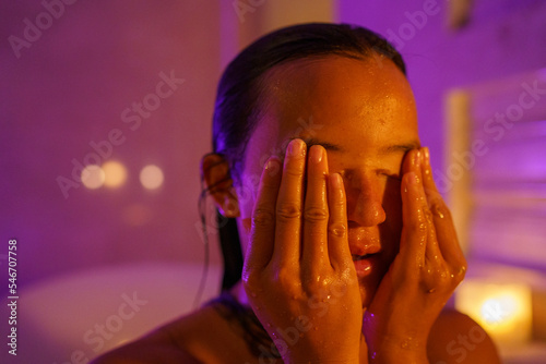 Woman covering eyes with wet hands while bathing