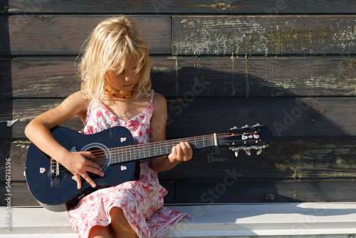 Girl playing guitar outside sunlit cottage photo