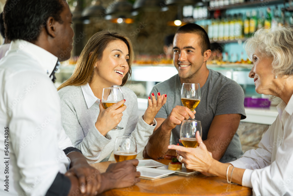 Group of cheerful friends drinking beer in bar and celebrating holidays. Focus on young woman