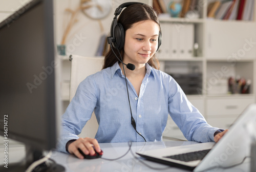 Positive dispatcher girl, who works in the office of a large company, sits at the workplace in front of the computer