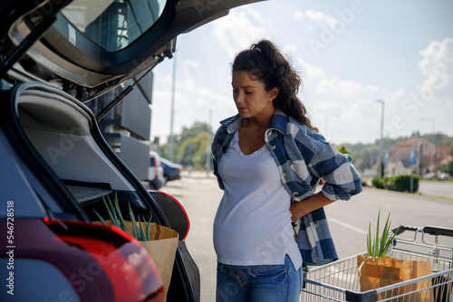 Pregnant woman pressing on aching back while loading shopping