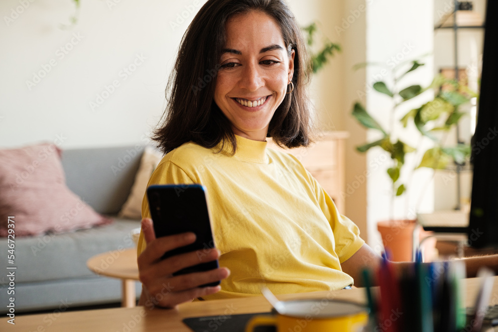 © Malquerida Studio/Stocksy - Smiling woman looking phone during work