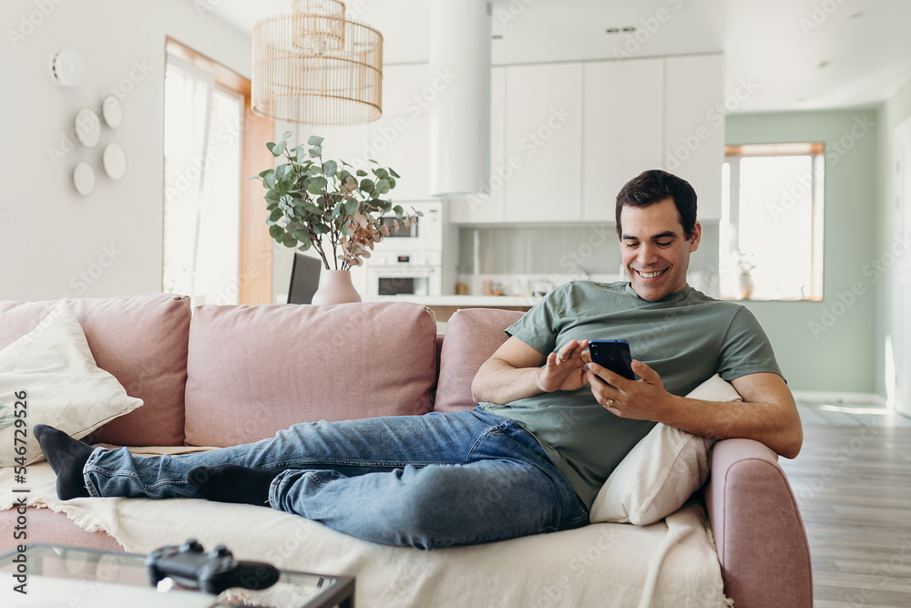 Happy Hispanic man using cellphone on couch Happy Hispanic man using cellphone on couch