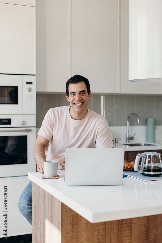 Cheerful Hispanic man sitting at table with laptop Cheerful Hispanic man sitting at table with laptop