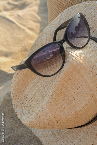 Hat with beautiful sunglasses on sandy beach, closeup