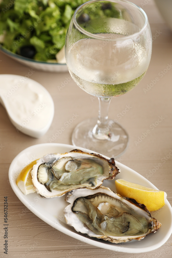 Plate of delicious raw oysters served with lemon and wine at wooden table Plate of delicious raw oysters served with lemon and wine at wooden table