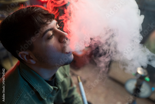 Young brunet exhaling hookah smoke