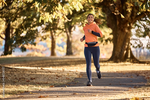 Young happy sportswoman running in park during autumn day.