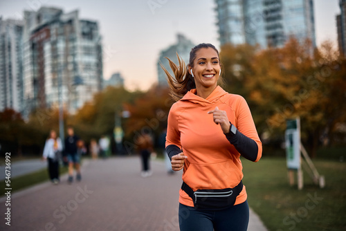 Fototapeta Happy sportswoman with earbuds running in park.