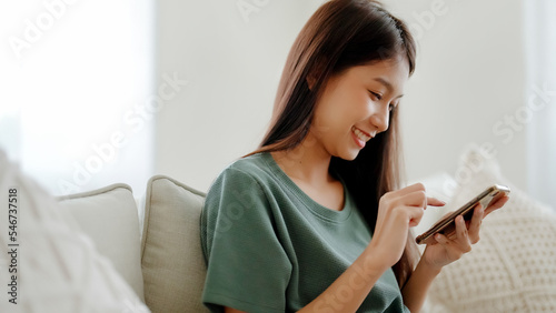 Obraz na plátně Happy young asian woman relax on comfortable couch at home texting messaging on