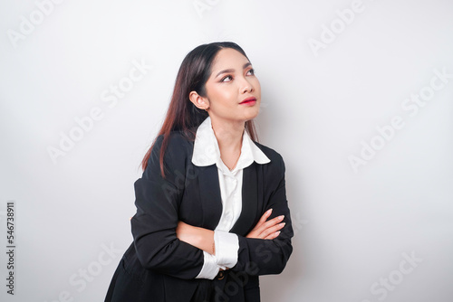 Portrait of a confident smiling Asian girl boss wearing black suit standing with arms folded and looking at the camera isolated over white background