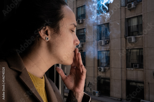 woman smokes tobacco at the window and throws the smoke outside photo
