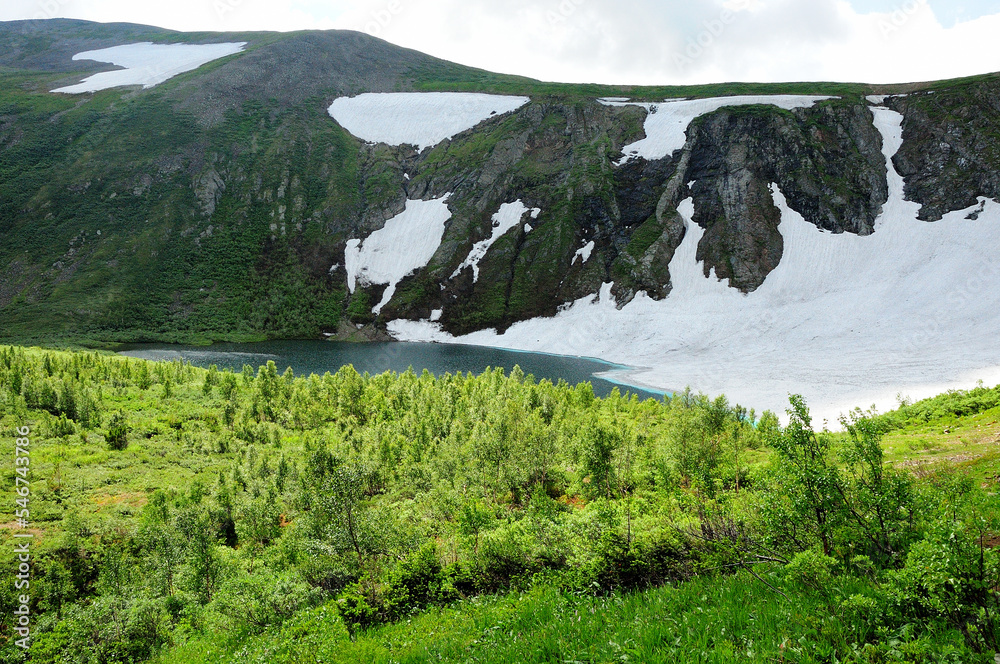 Obraz premium A picturesque lake with turquoise water at the foot of a high cliff with the remains of snow on the slopes.