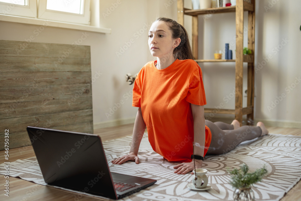 Woman in a bright clothes on the floor in front of a laptop is doing yoga using a video lesson Woman in a bright clothes on the floor in front of a laptop is doing yoga using a video lesson