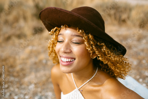 Pretty girl with hat and curly hair smiling outdoors in sunlight