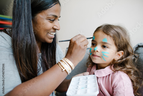 Woman paint a daughter's face with blue paint