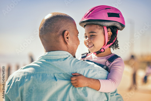 Family, love and girl with dad and helmet for safety before cycling together at park outdoors, happy and hug. Children, learning and father embrace daughter, bonding and talking before riding a bike