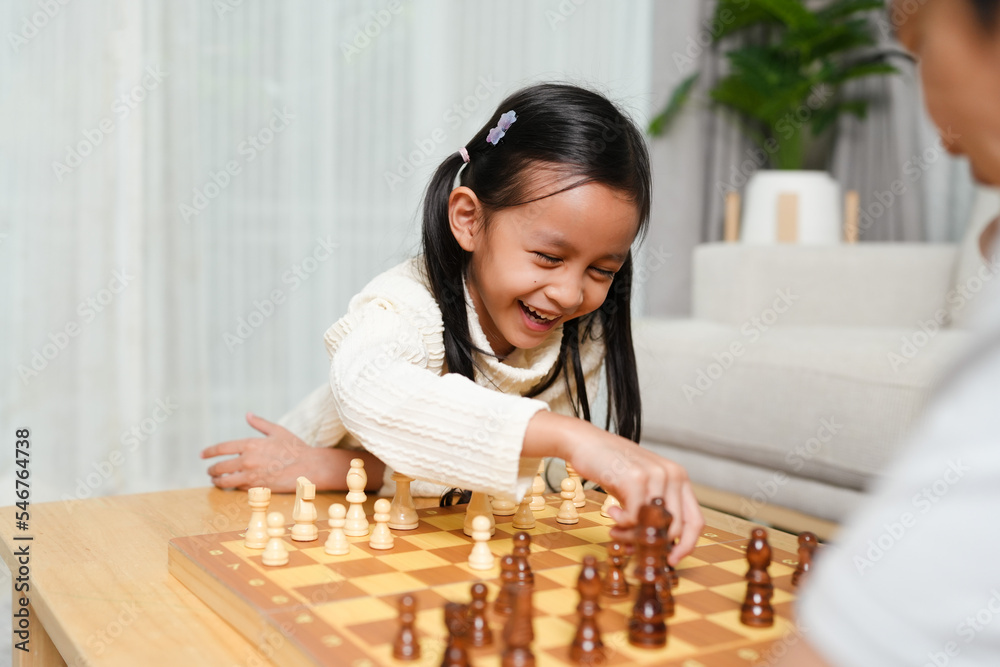 Asian little girl is playing chess board game withe father in the living room with happy moment. Concept of kid learning, strategy, education, friendship, competition, lose and win. Asian little girl is playing chess board game withe father in the living room with happy moment. Concept of kid learning, strategy, education, friendship, competition, lose and win.
