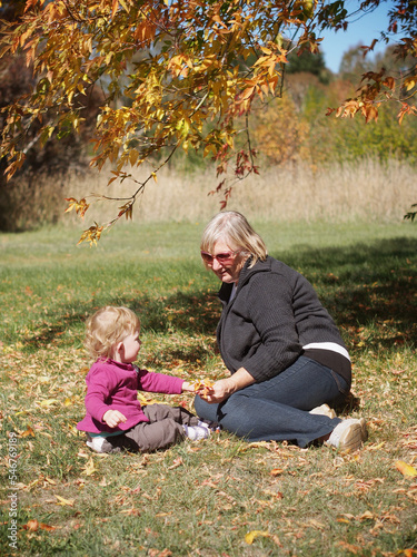 Young two year old girl sitting playing in fall autumn leaves  with grandmother.