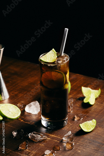 Cuba libre cocktail cold and refreshing drink for summer days on a wooden table with ice and slices of lemons