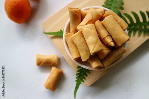Sumpia or mini crunchy spring rolls on white plate and wooden cutting board. Indonesian homemade crispy fried snack, Wrapped by Kulit Lumpia and filled with Ebi or Shredded Shrimp. photo