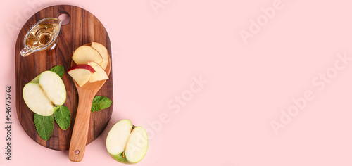 Wooden board with gravy boat of apple cider vinegar and fruits on pink background with space for text