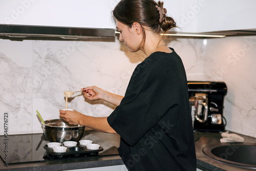 Pastry chef filling paper cupcake molds with dough