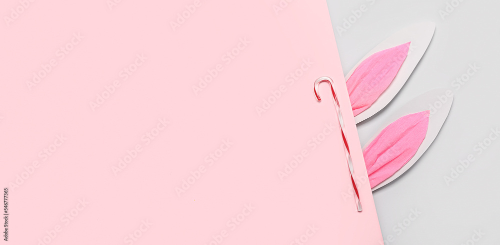 Paper bunny ears with candy cane on pink and grey background