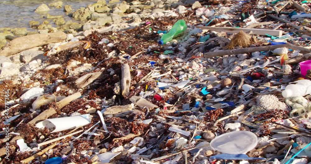 Wide overview pan of plastic trash debris littered on rocky beach in Caribbean Wide overview pan of plastic trash debris littered on rocky beach in Caribbean