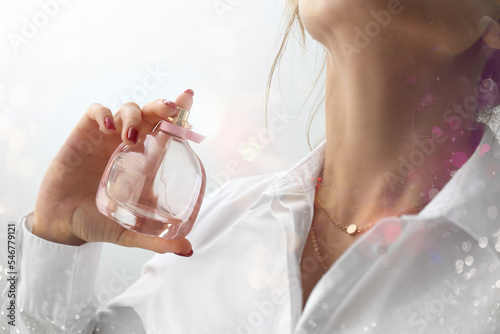 Woman with bottle of luxury perfume on light background, closeup