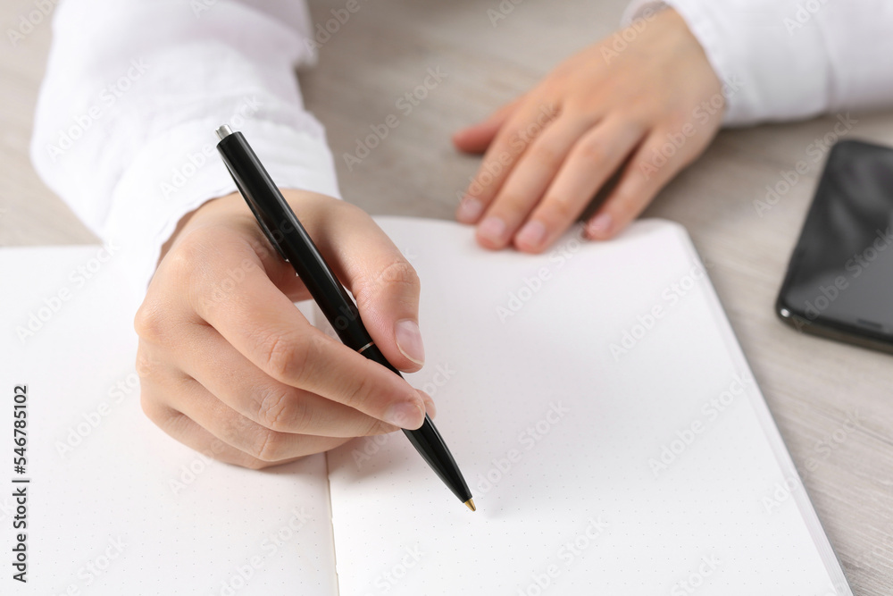 Woman writing in notebook at wooden table, closeup Woman writing in notebook at wooden table, closeup