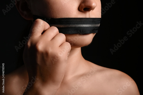 фотографія Young woman with zipper on her mouth against dark background, closeup