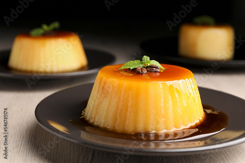 Plate of delicious caramel pudding with coffee beans and mint on white wooden table, closeup