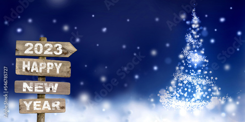 2023 happy new year written on wooden signpost and abstract christmas tree in snow photo