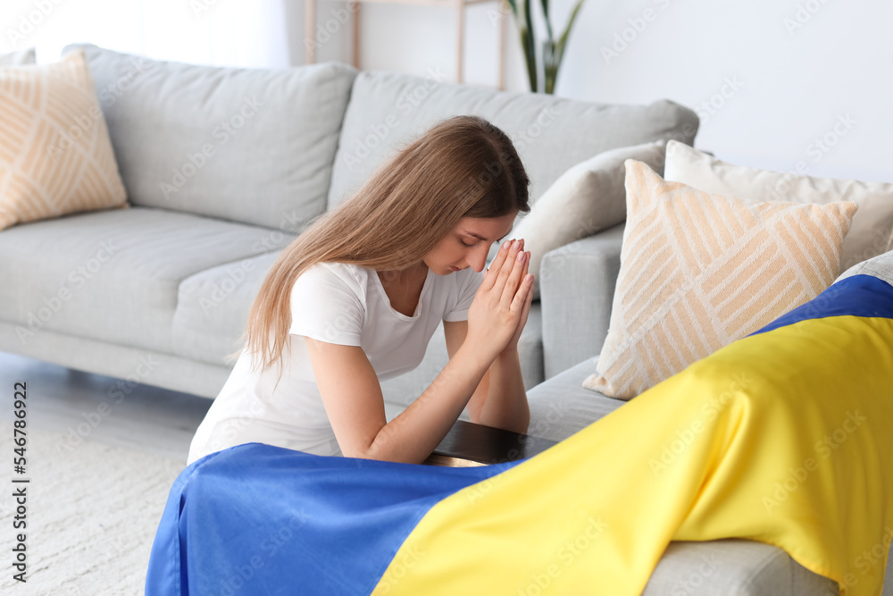 Young woman with Ukrainian flag praying at home Young woman with Ukrainian flag praying at home